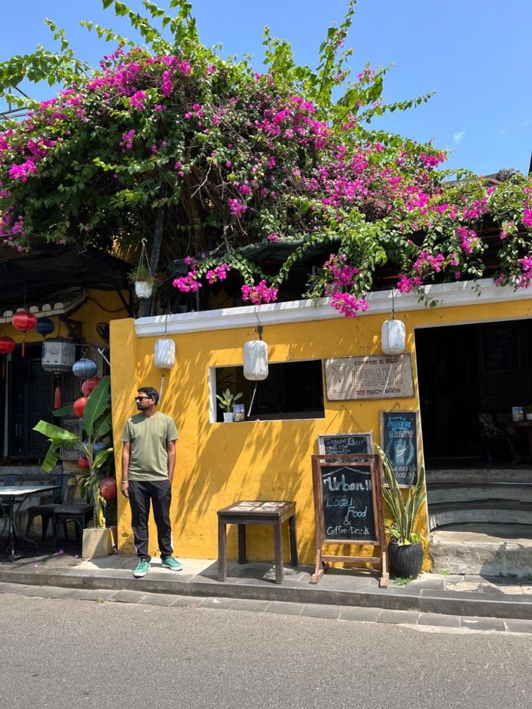 Ram by a yellow café wall under bougainvillea in Hoi An